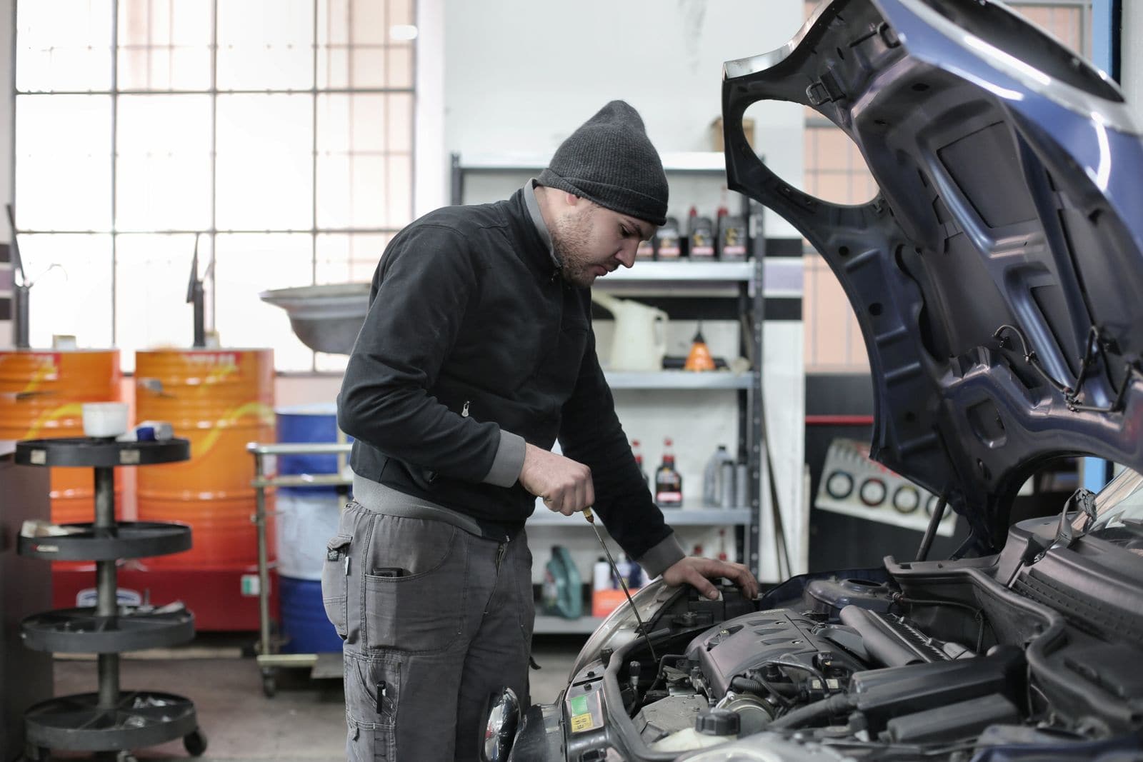 Technician checking the oil level under the open hood of a car in an independent repair shop