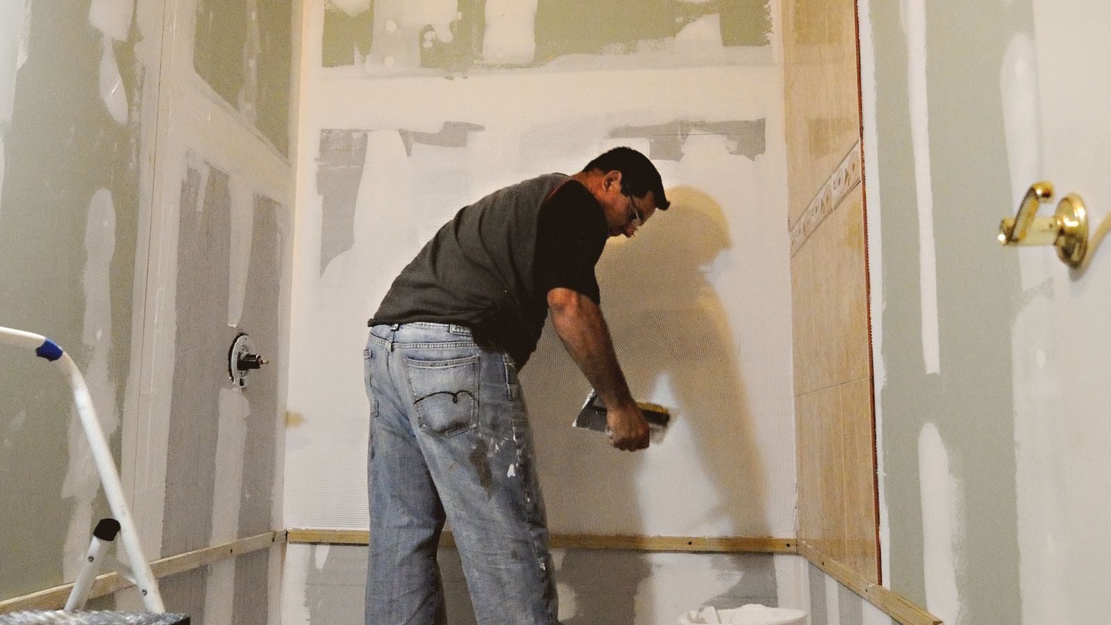 Remodeler finishing drywall in a gutted bathroom with the plumbing roughed in