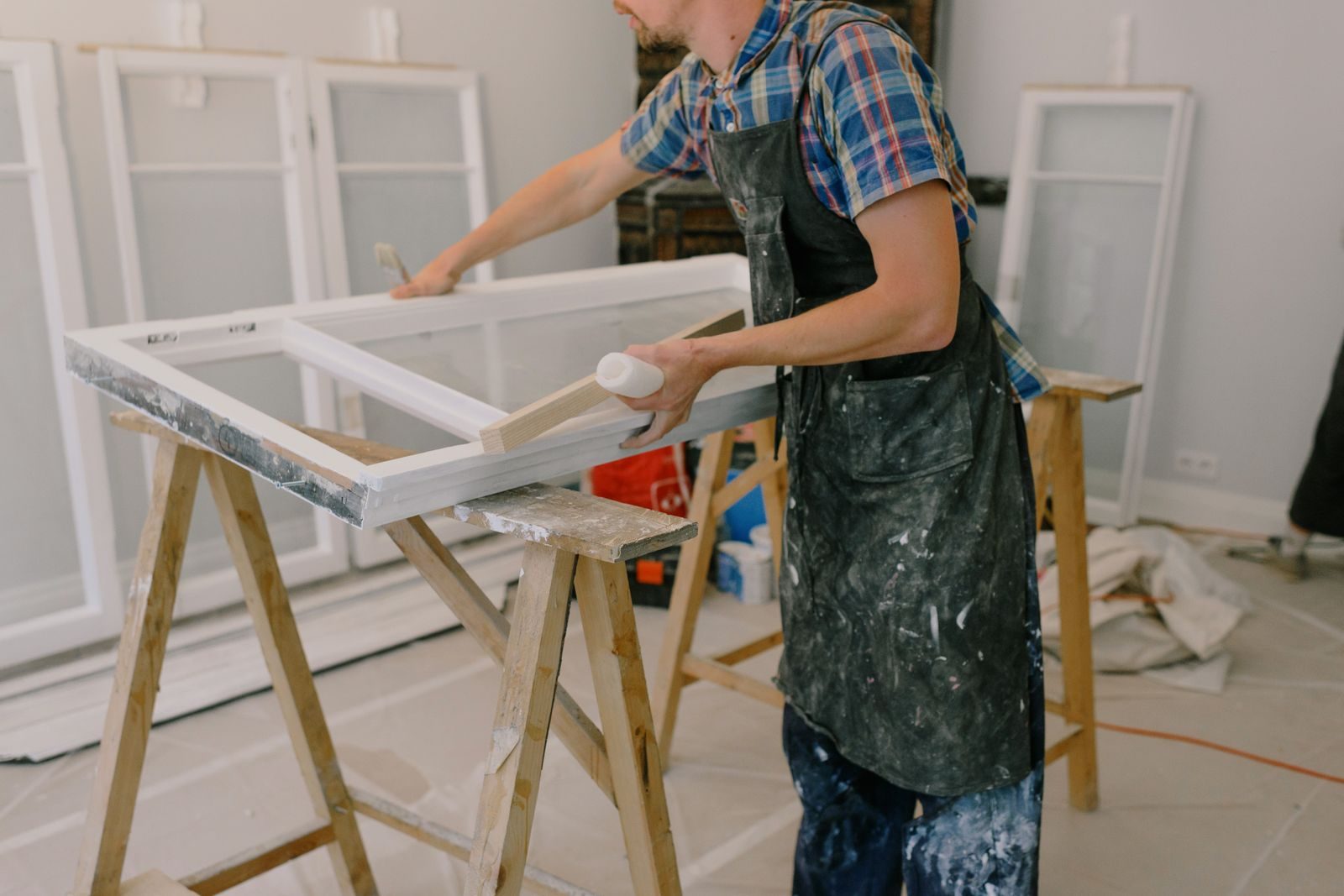 Carpenter sanding a white window frame laid across sawhorses