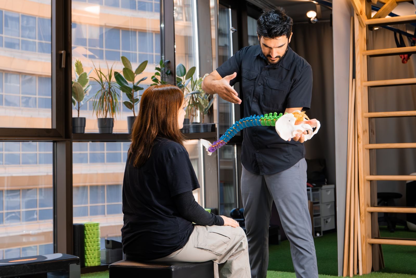 Chiropractor explaining a spine model to a seated patient during a consultation