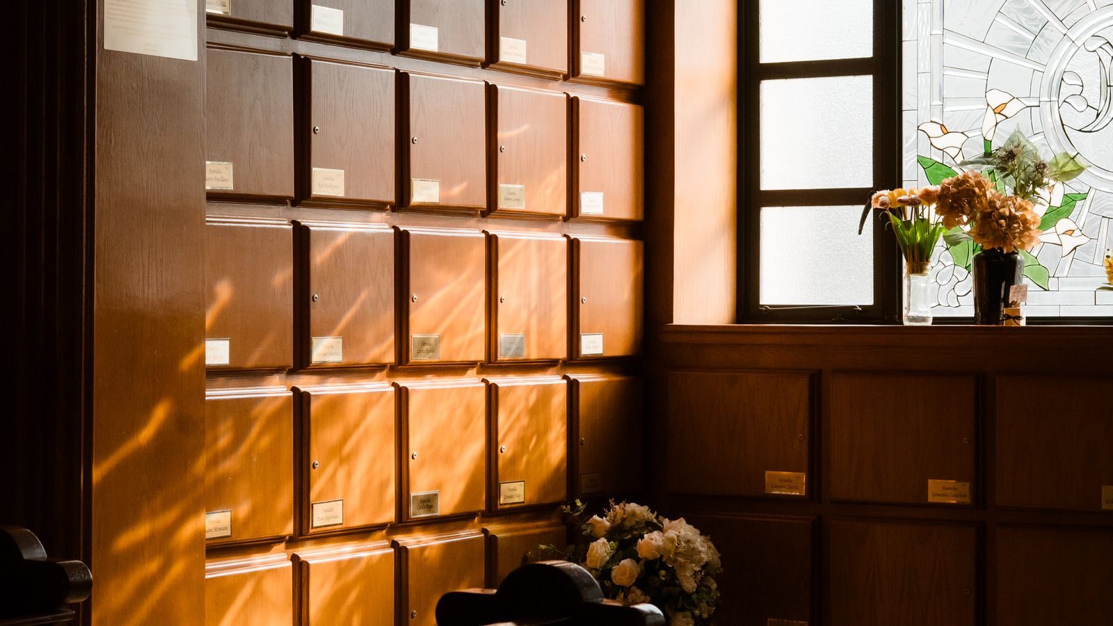 Sunlight falling across a wall of columbarium niches with flowers on a ledge