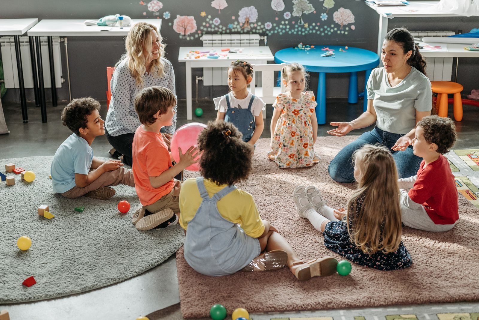 Two teachers leading circle time with a group of young children on a classroom rug