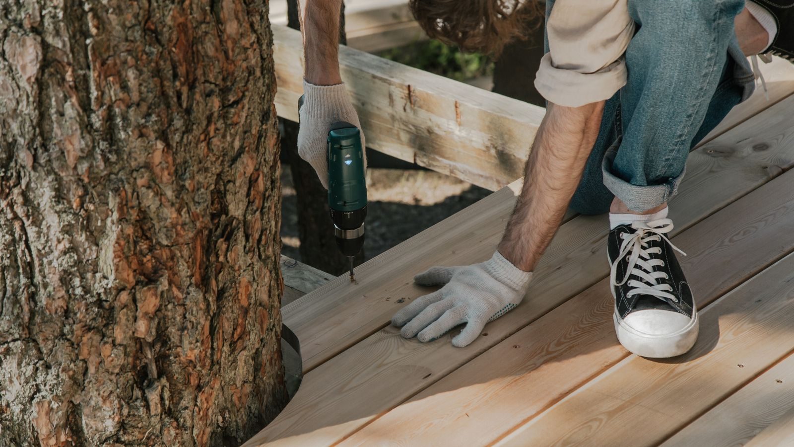 Carpenter fastening deck boards beside a tree