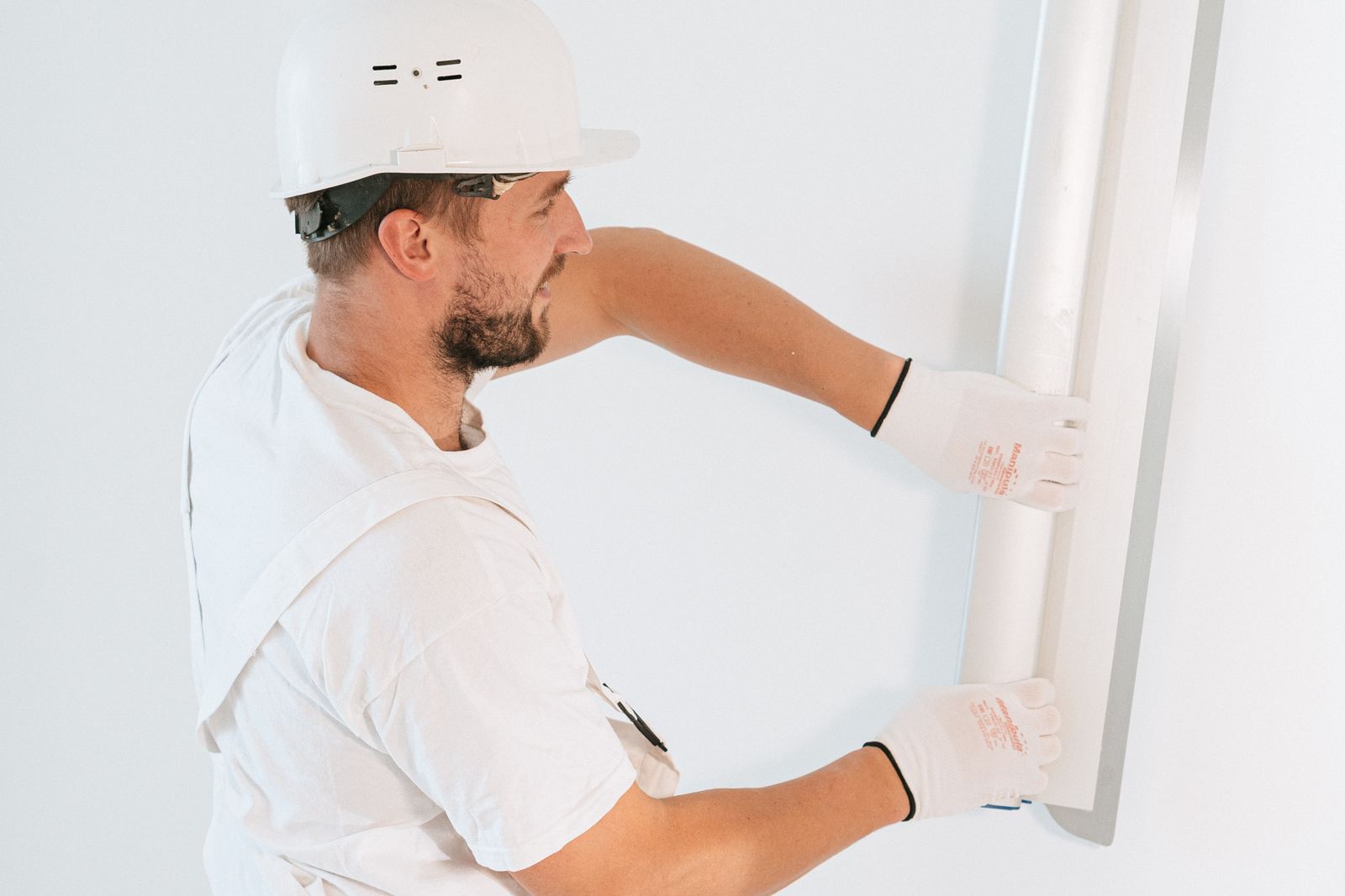 Worker in a hard hat lifting a drywall sheet into place