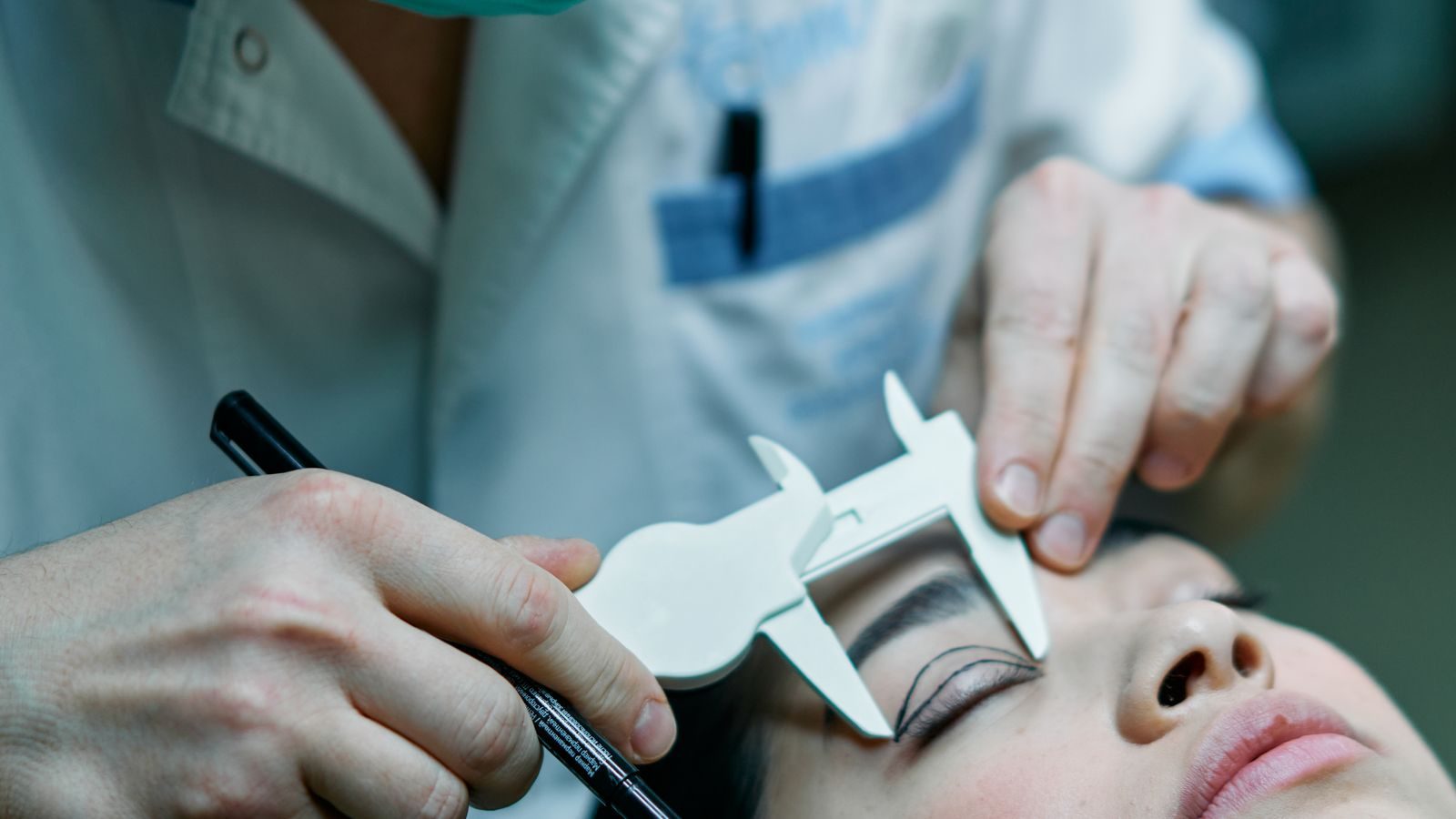 Surgeon measuring a patient's eyelid with a caliper before blepharoplasty