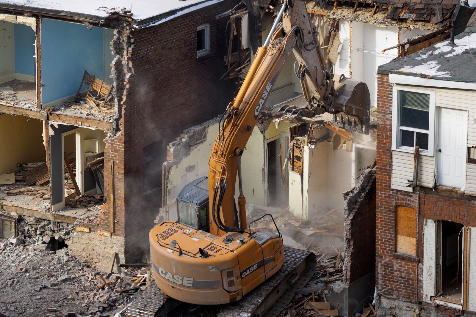 Excavator tearing down the wall of an old brick house