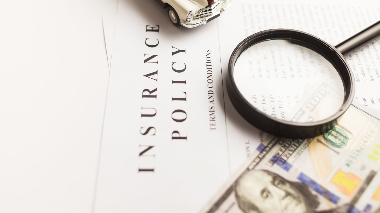 Insurance policy document under a magnifying glass beside a toy car