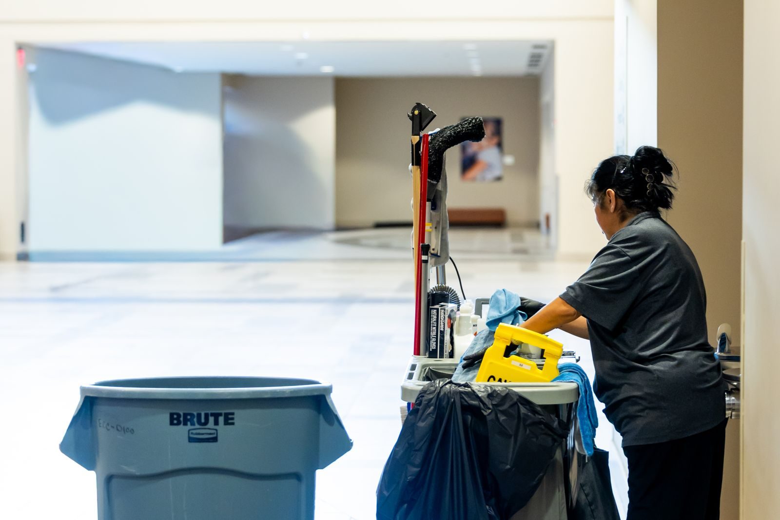 Janitor restocking a cleaning cart in a long office hallway