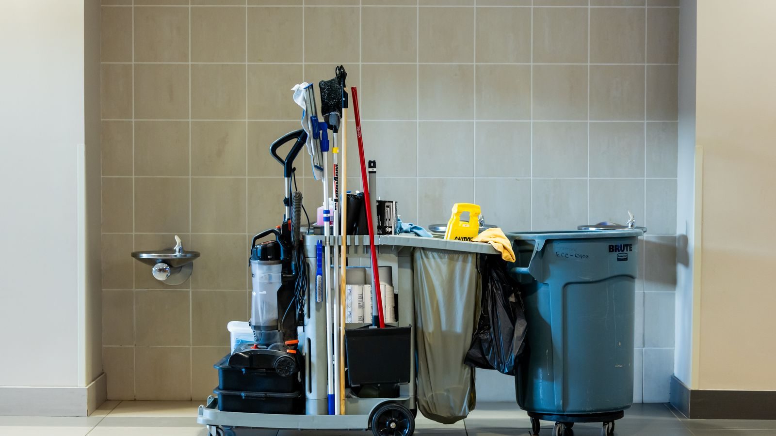 Janitorial cart with mops, bins and supplies parked in an office corridor