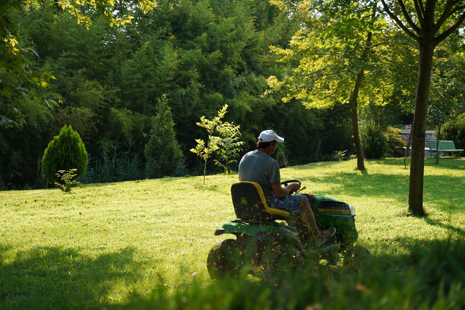 Operator on a ride-on mower cutting a sunlit lawn