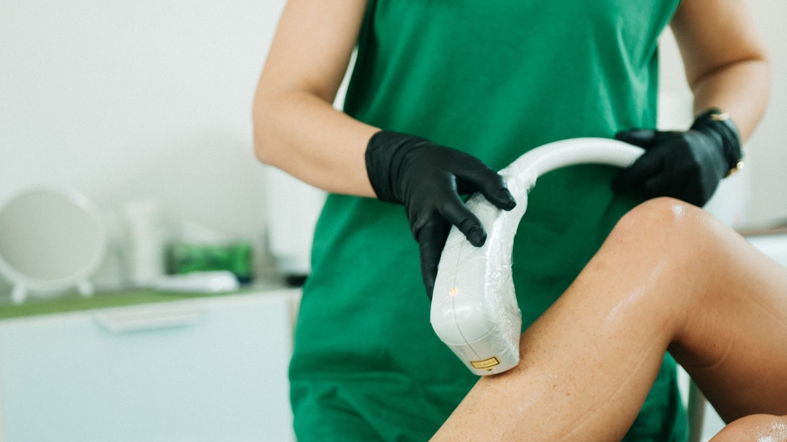Provider in green scrubs performing a laser treatment on a patient