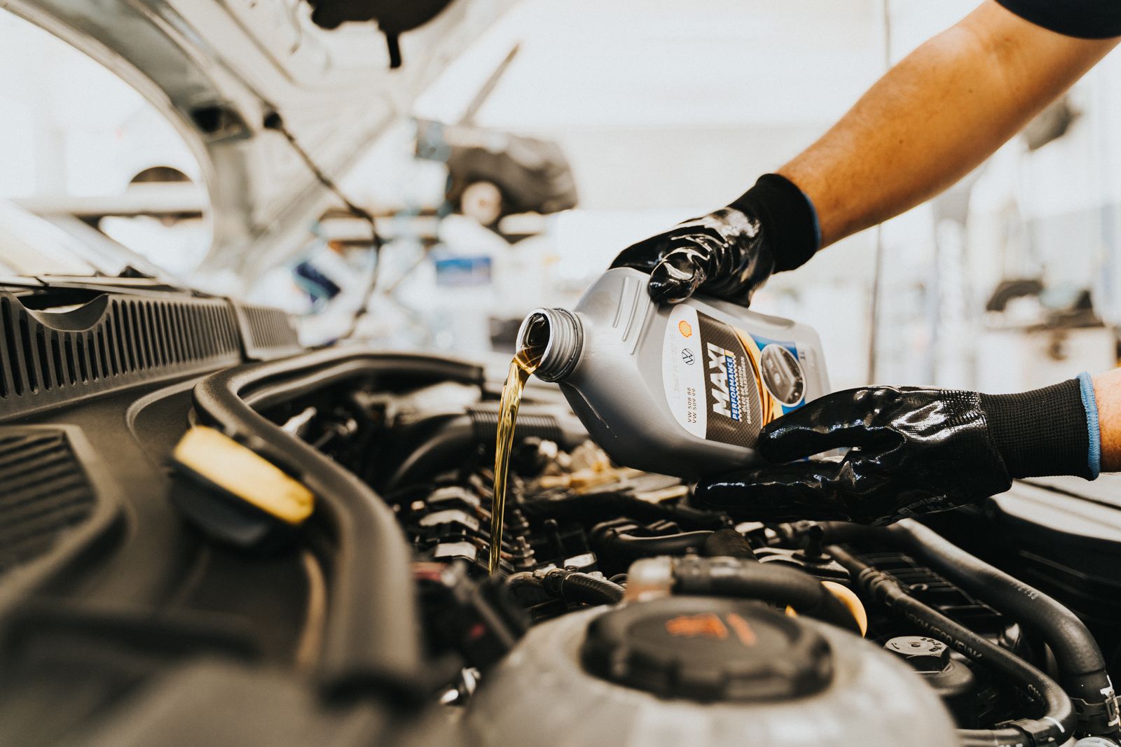 Mechanic pouring engine oil under the hood of a car