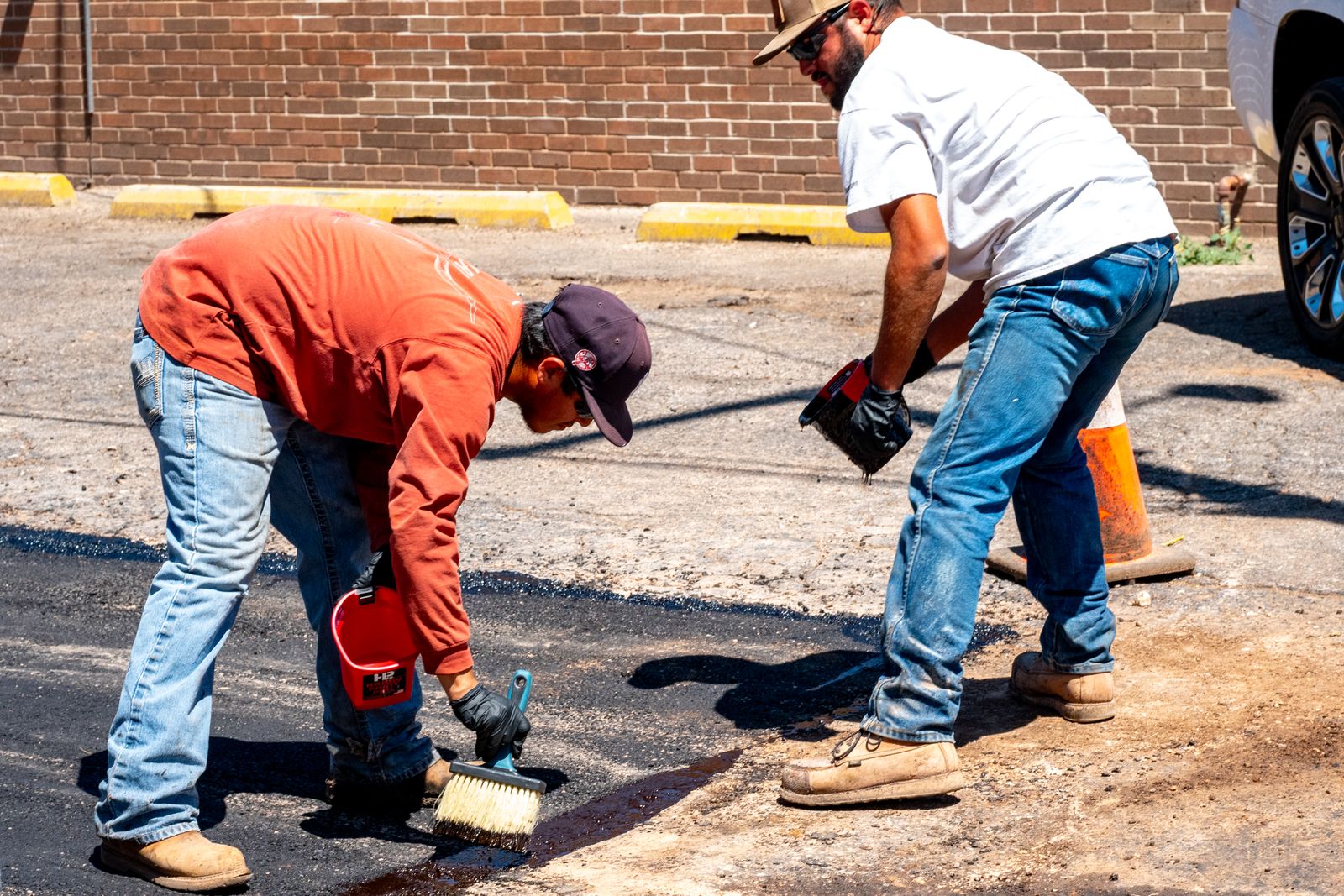 Two workers repairing an asphalt surface on a sunny day