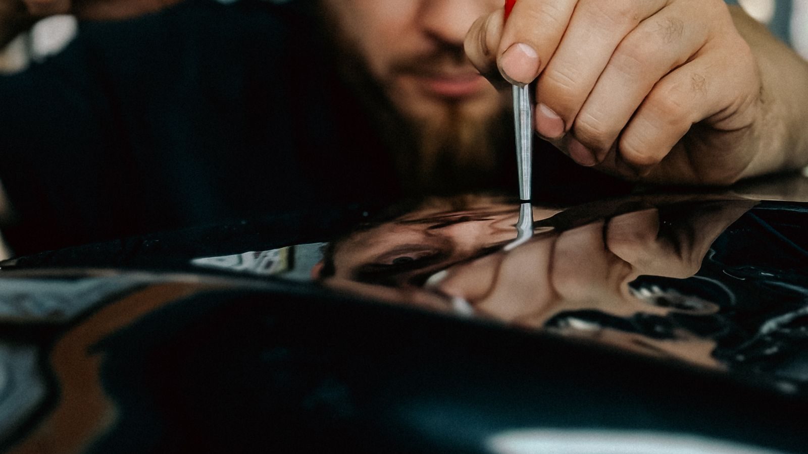 Technician working a dent out of a dark panel with a paintless dent repair tool