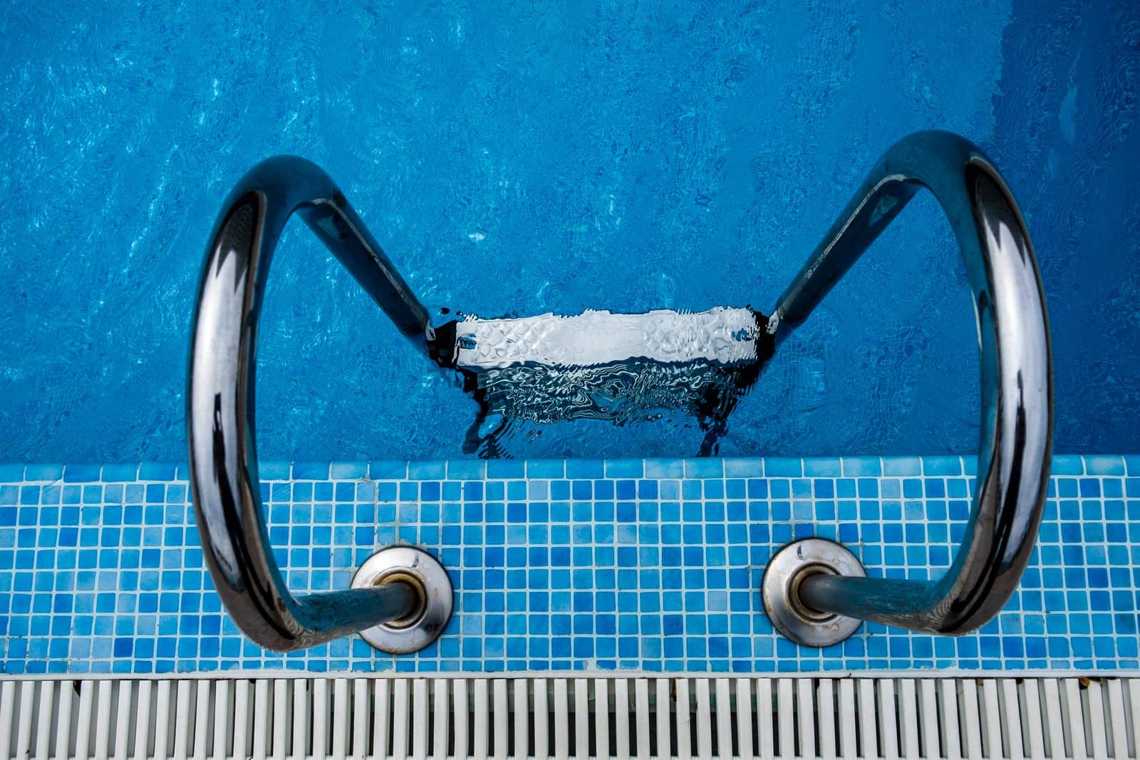 Stainless steel ladder and clear blue water at the edge of a maintained swimming pool