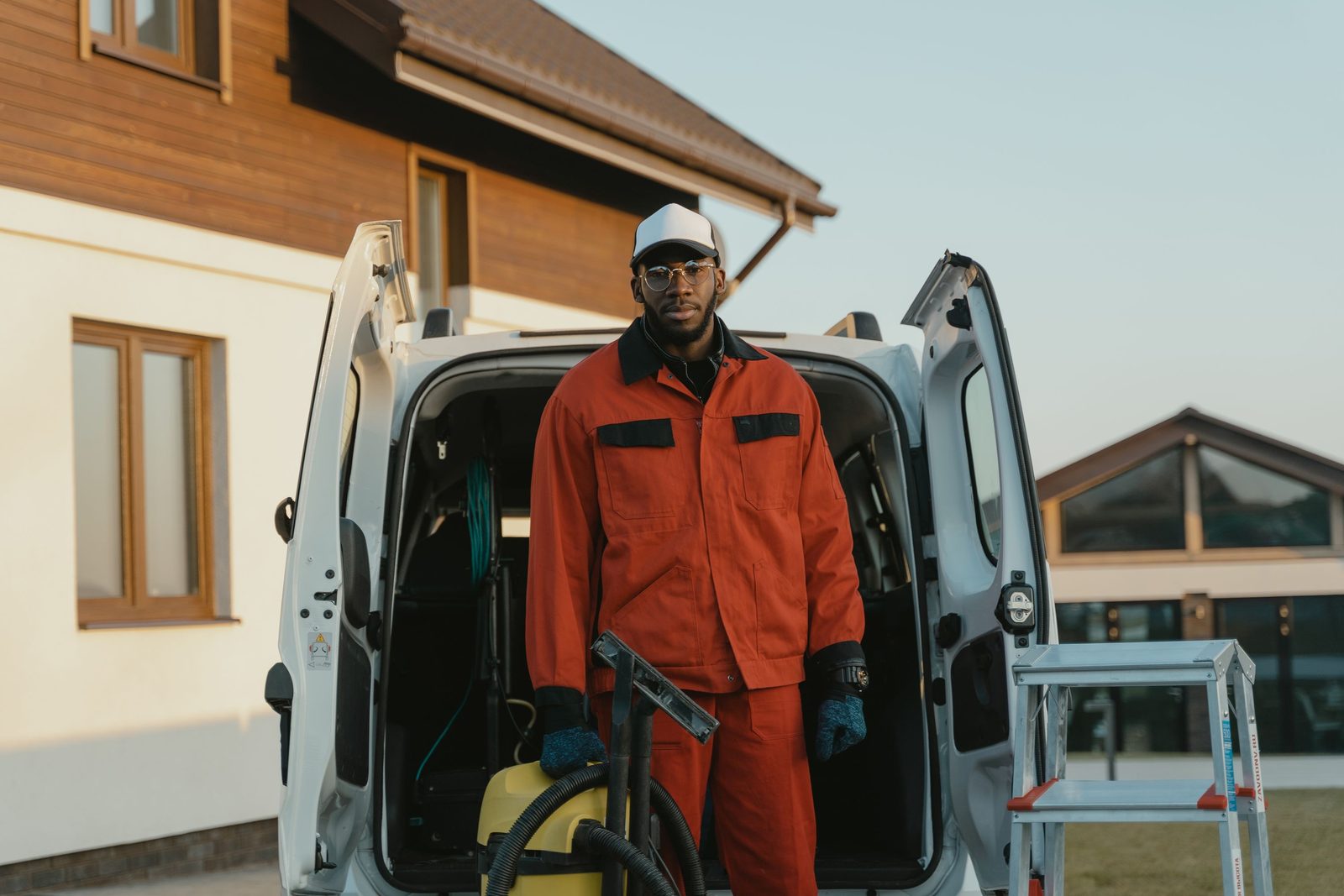 Exterior cleaning contractor standing at the open rear of his work van with his equipment outside a house