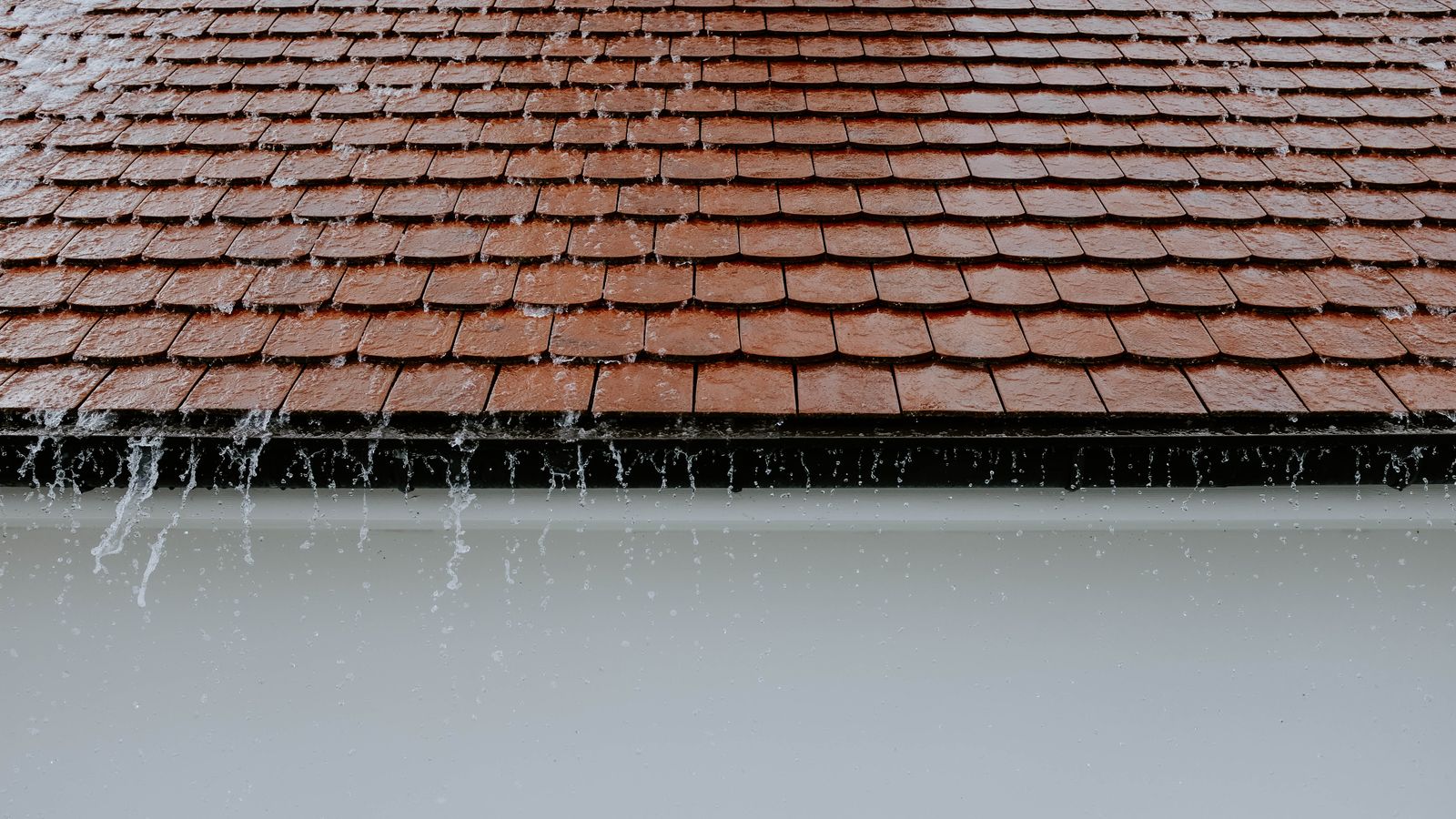 Rain overflowing a clogged gutter below a tile roof