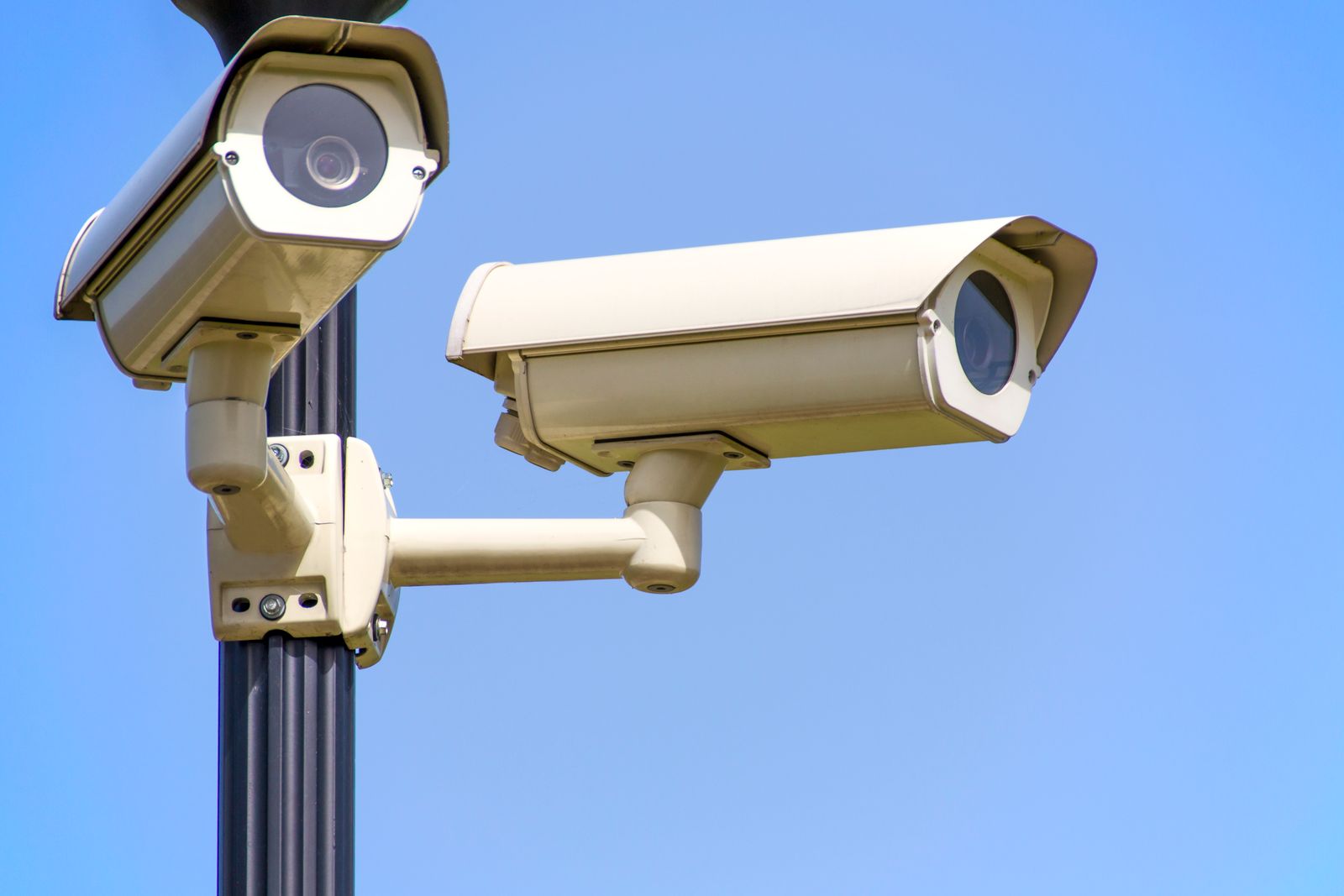 Two outdoor security cameras mounted on a pole against the sky