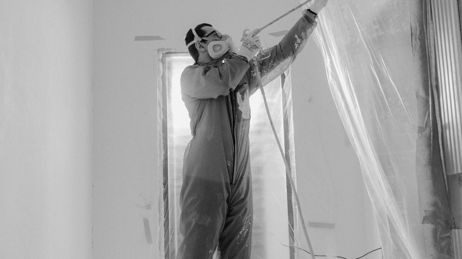 Worker in a respirator and suit spraying a wall during a renovation