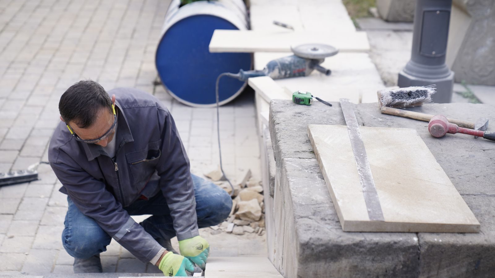 Mason in safety glasses setting stone pavers outdoors