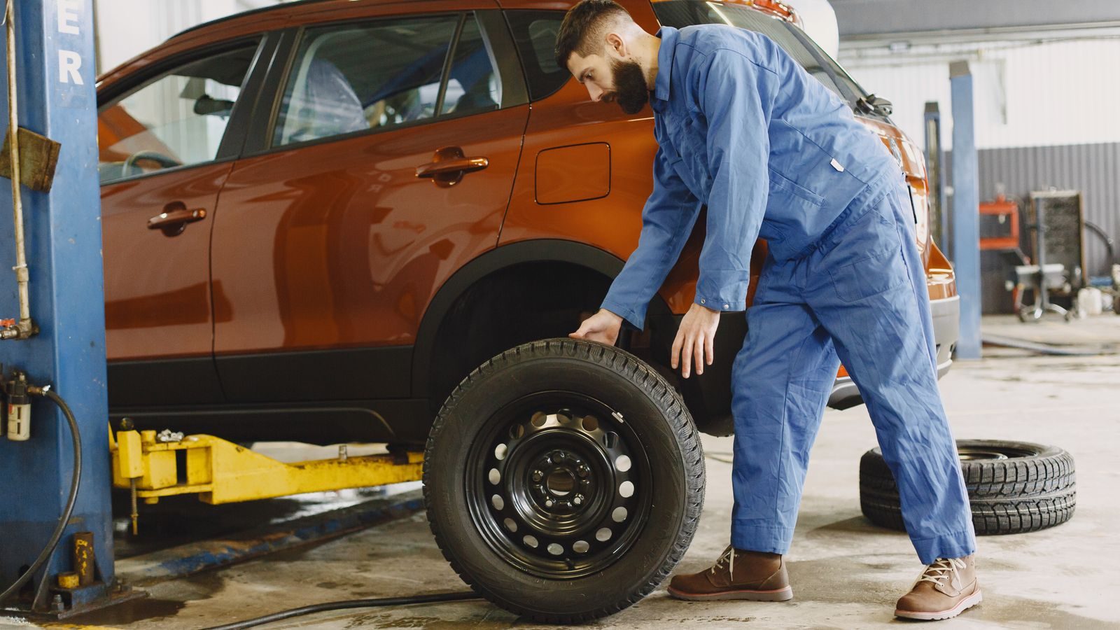 Mechanic in blue coveralls fitting a wheel to a red SUV on a lift