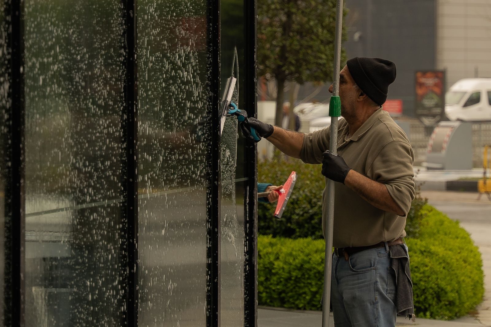 Window cleaner squeegeeing a storefront glass pane with a pole