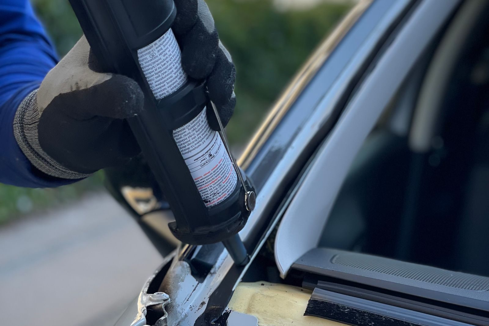 Technician in gloves running a bead of urethane along a windshield frame
