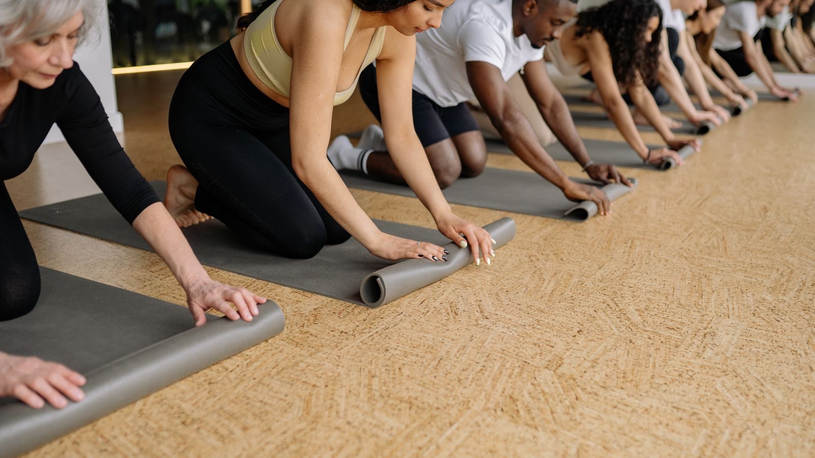 Students rolling up their mats in a row at the end of a studio class